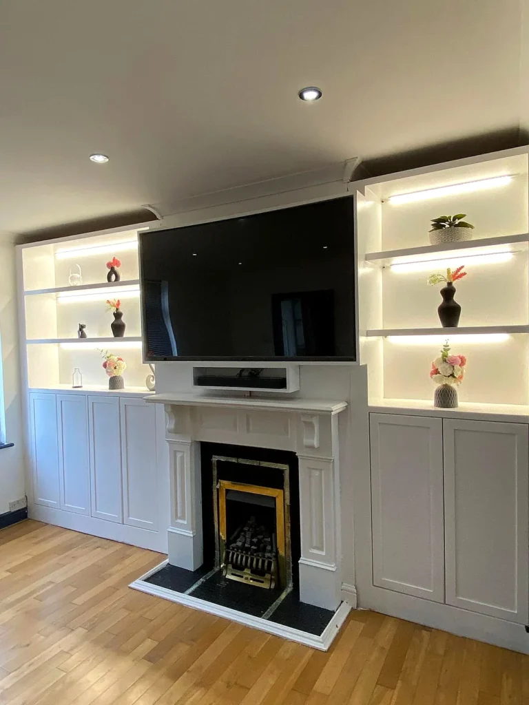 Completed white fitted media wall with LED-lit shelving either side of a fireplace