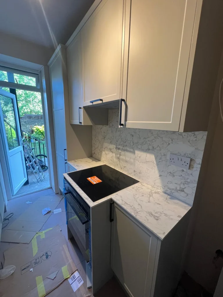 Marble-effect worktop and hob being fitted in a shaker kitchen, protective film still in place