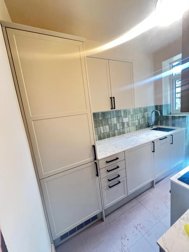 Completed shaker kitchen with sage green tiles, marble-effect worktop and black handles