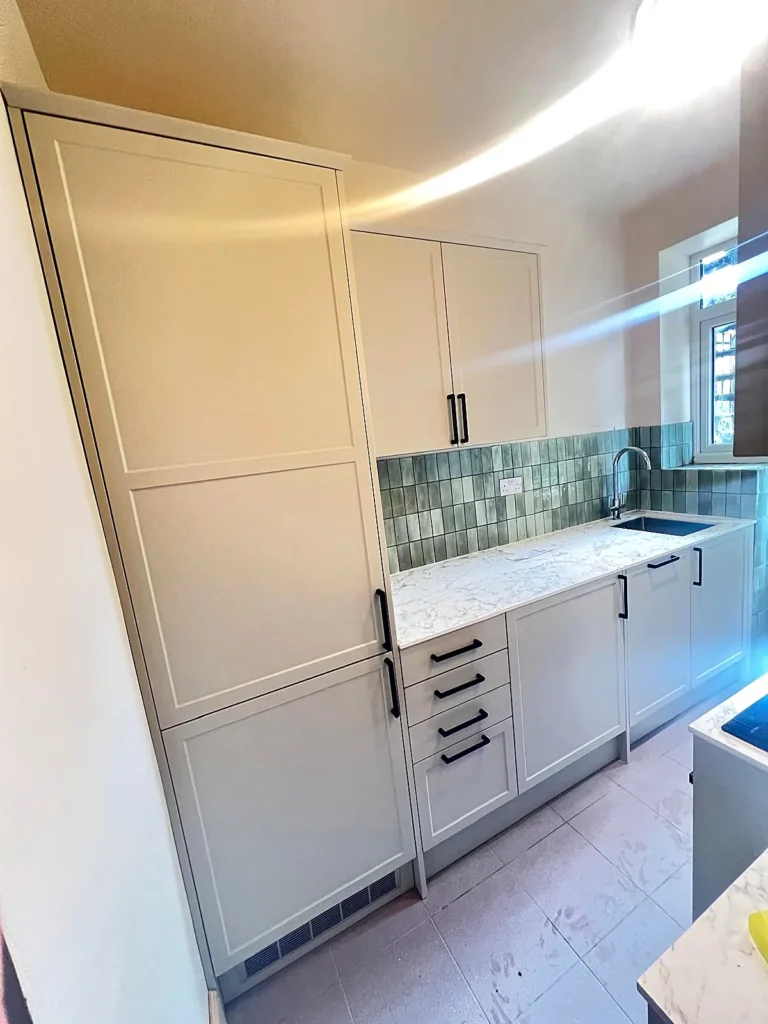 Shaker kitchen with tall larder units, green tiled splashback and marble-effect worktop